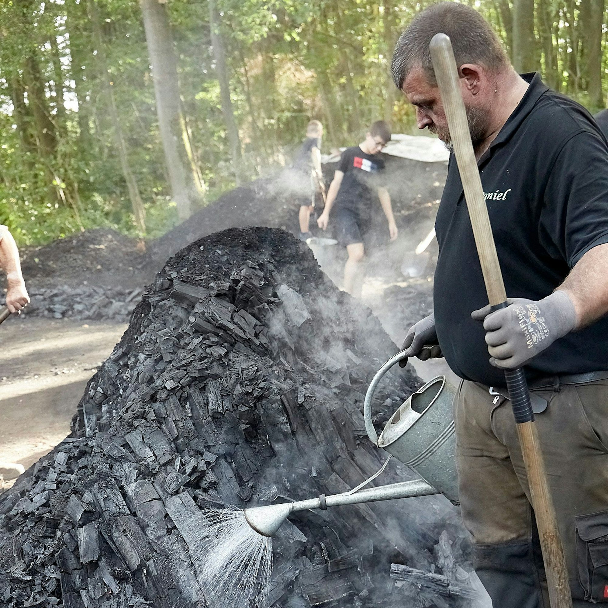 Daniel Linden gießt mit einer Gießkanne Wasser auf schwarze Kohle.