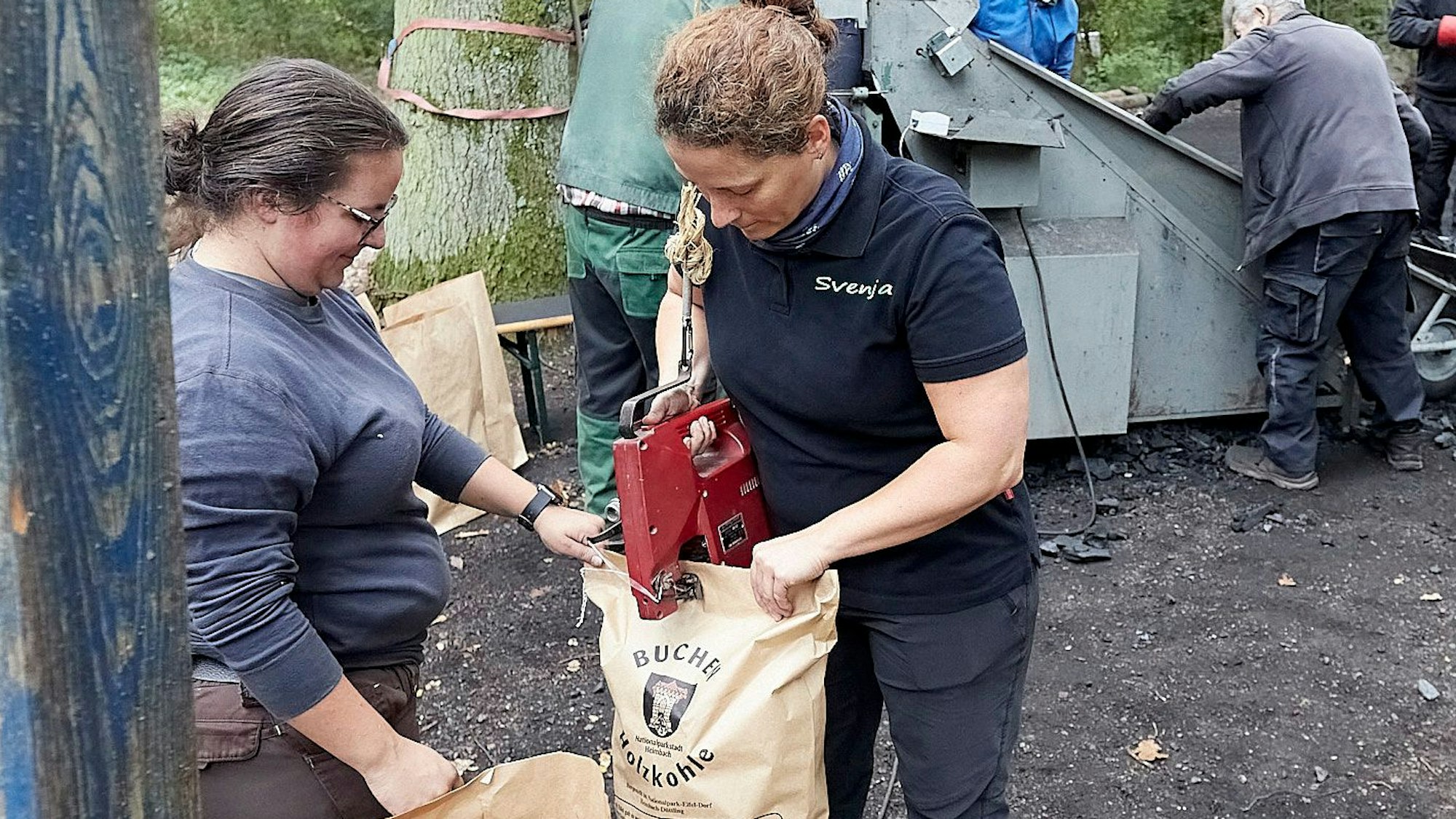 Zwei Frauen verpacken Holzkohle in großen Papiertüten.