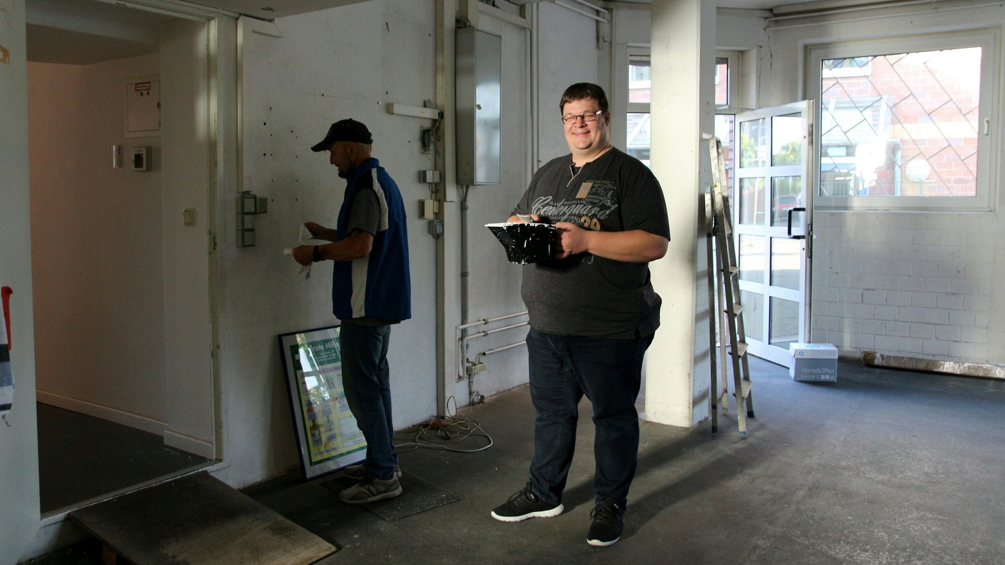 Ein Arbeiter streicht eine Wand, ein anderer rührt Farbe an.