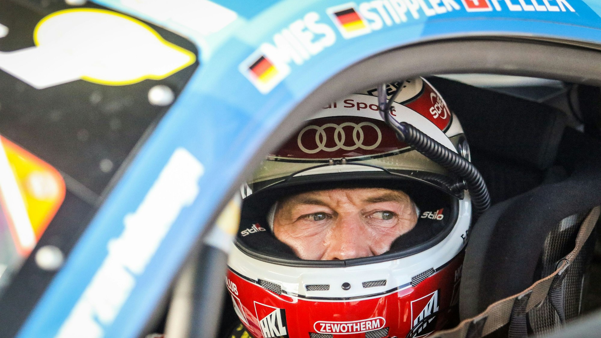 Rennfahrer Frank Stippler sitzt, mit geöffnetem Visier, in seinem Rennwagen.