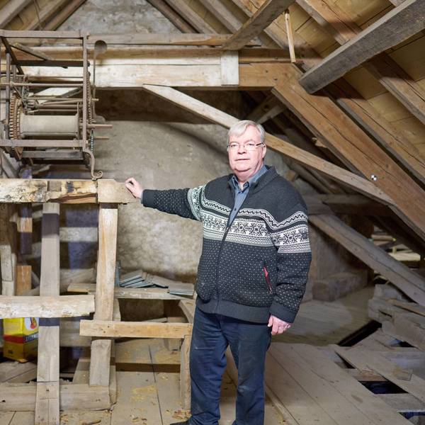 Helmut J. Kirfel steht vor einem Holzgerüst, auf der die Reste einer Uhr aus dem 15. Jahrhundert auf dem Dachboden der Steinfelder Basilika zu sehen sind.