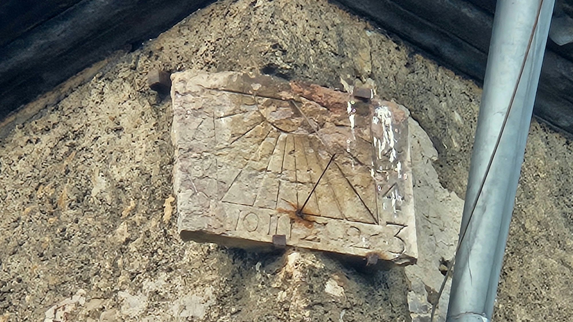 Zu sehen ist eine Sonnenuhr, die unter einem schmalen Dachvorstand angebracht ist.