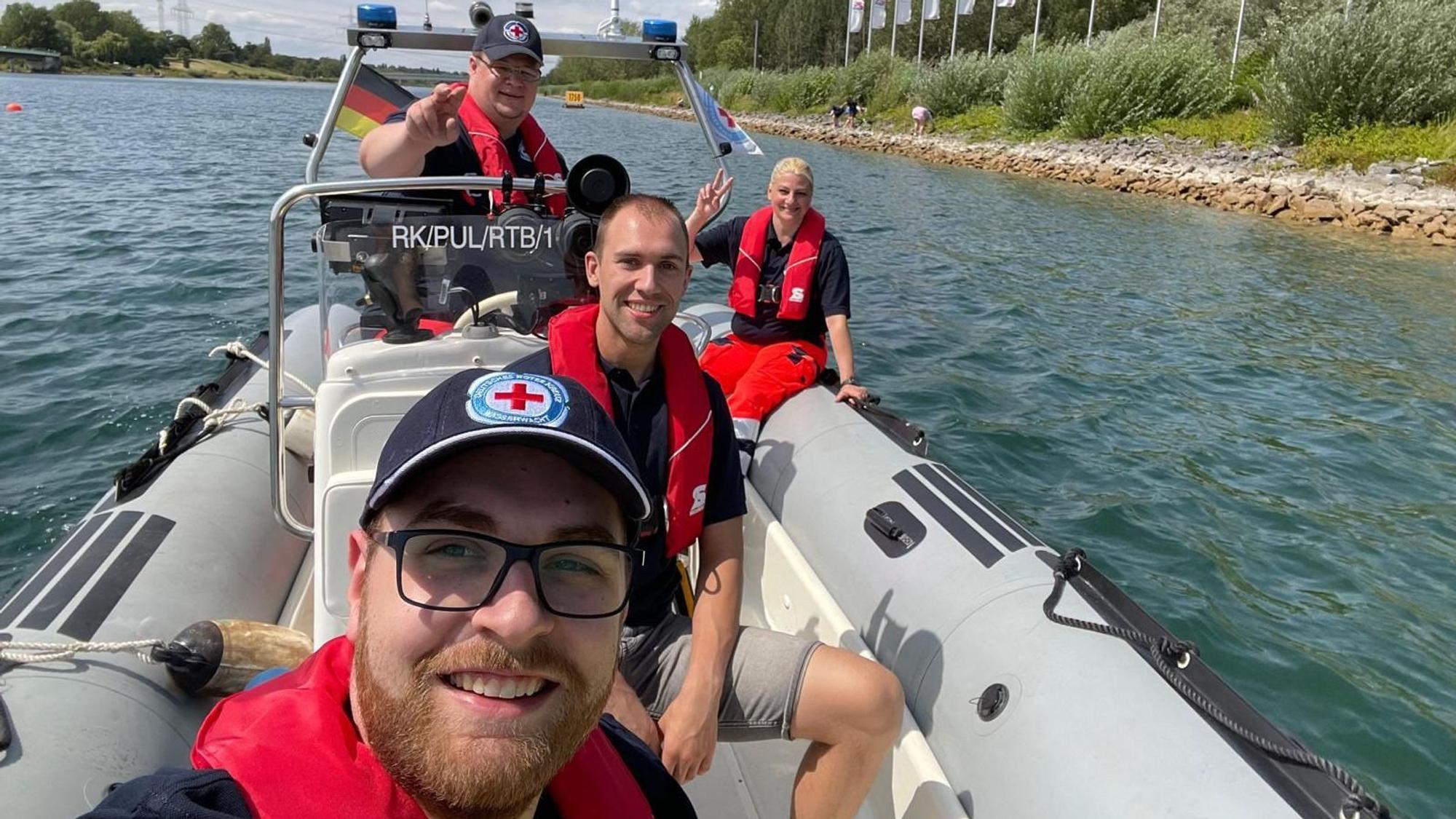 Vier Mitglieder der Wasserwacht sitzen in einem Rettungsboot, fürs Foto lächeln sie in die Kamera.