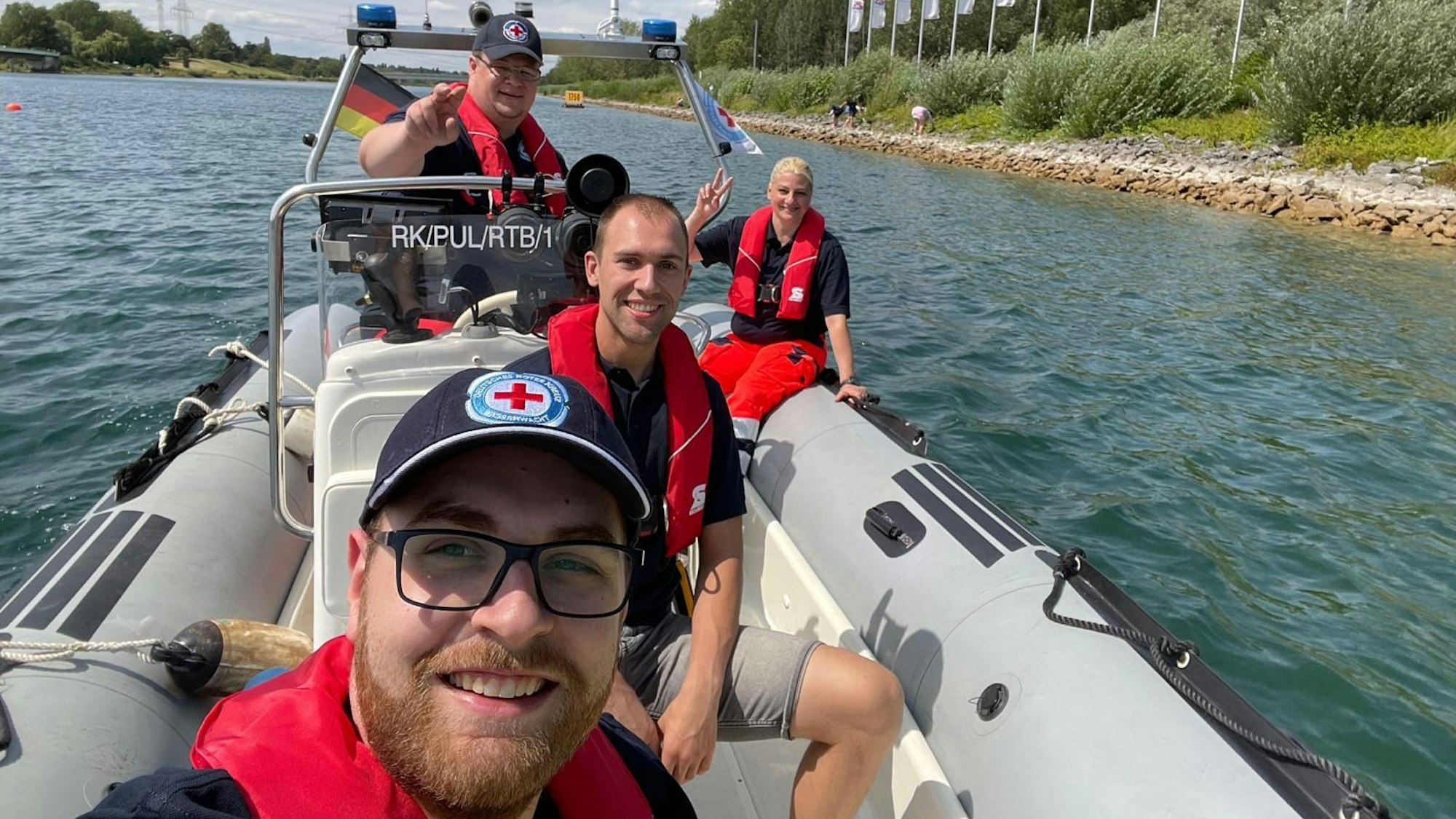 Vier Mitglieder der Wasserwacht sitzen in einem Rettungsboot, fürs Foto lächeln sie in die Kamera.