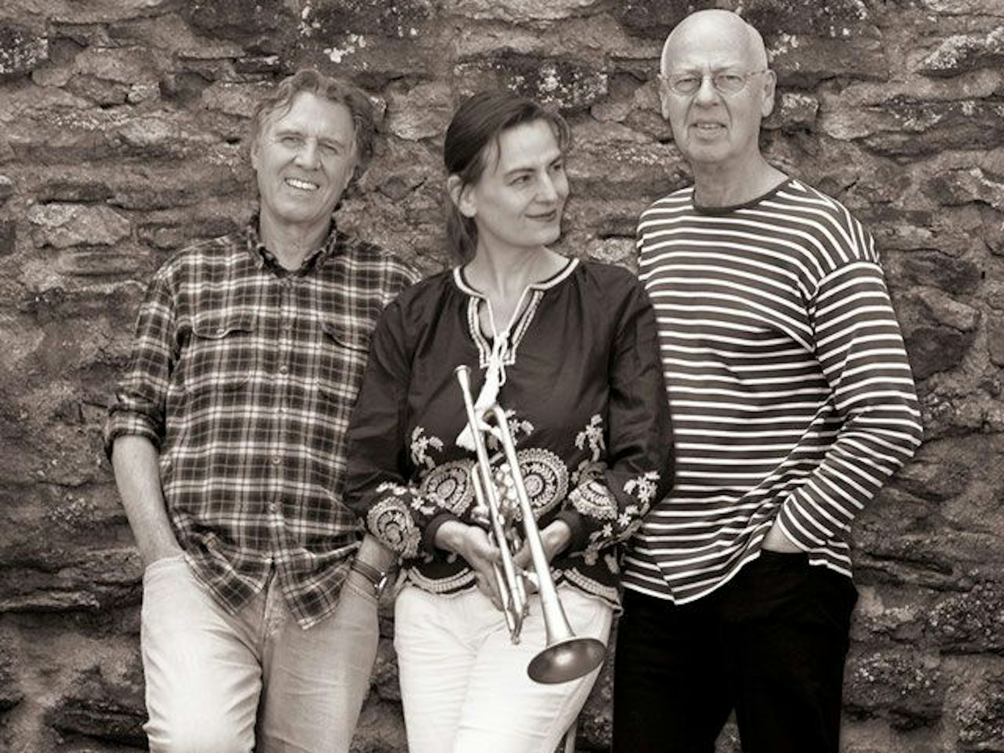Der Schriftsteller Norbert Scheuer (l.), die Trompeterin Susanne Riemer und der Bassist Wilhelm Geschwind stehen vor einer Mauer.