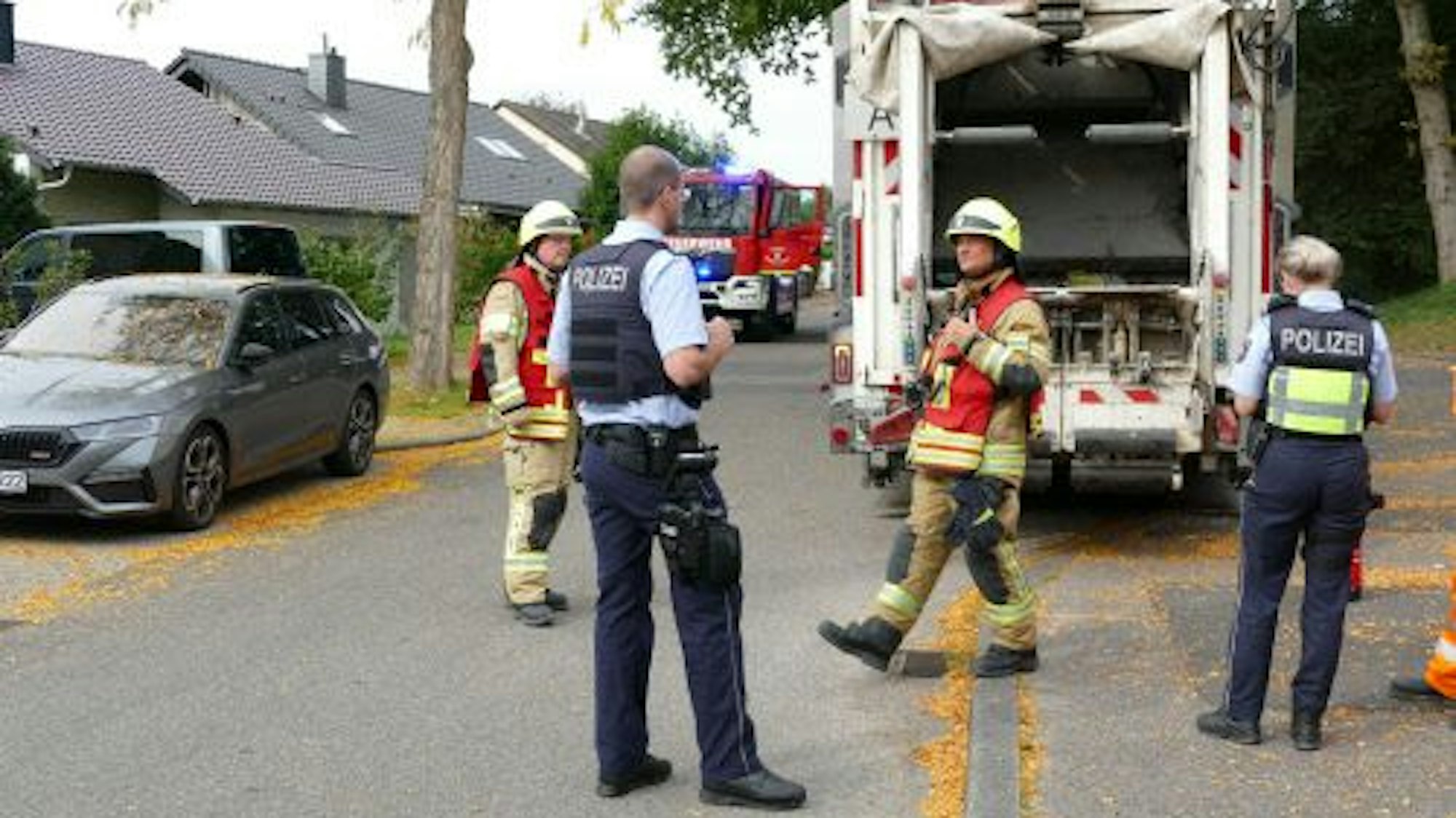 Feuerwehrleute und Polizeibeamte hinter dem Müllwagen.