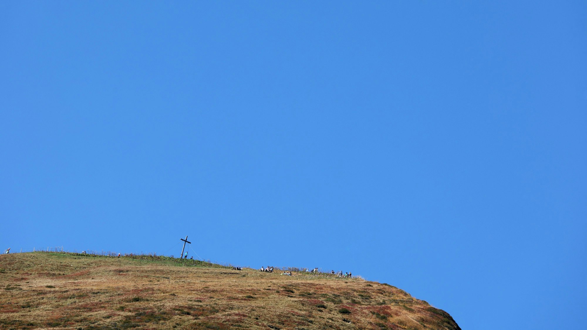 Auf einer Bergspitze steht ein Kreuz unter einem wolkenlosen Himmel. (Symbolbild)