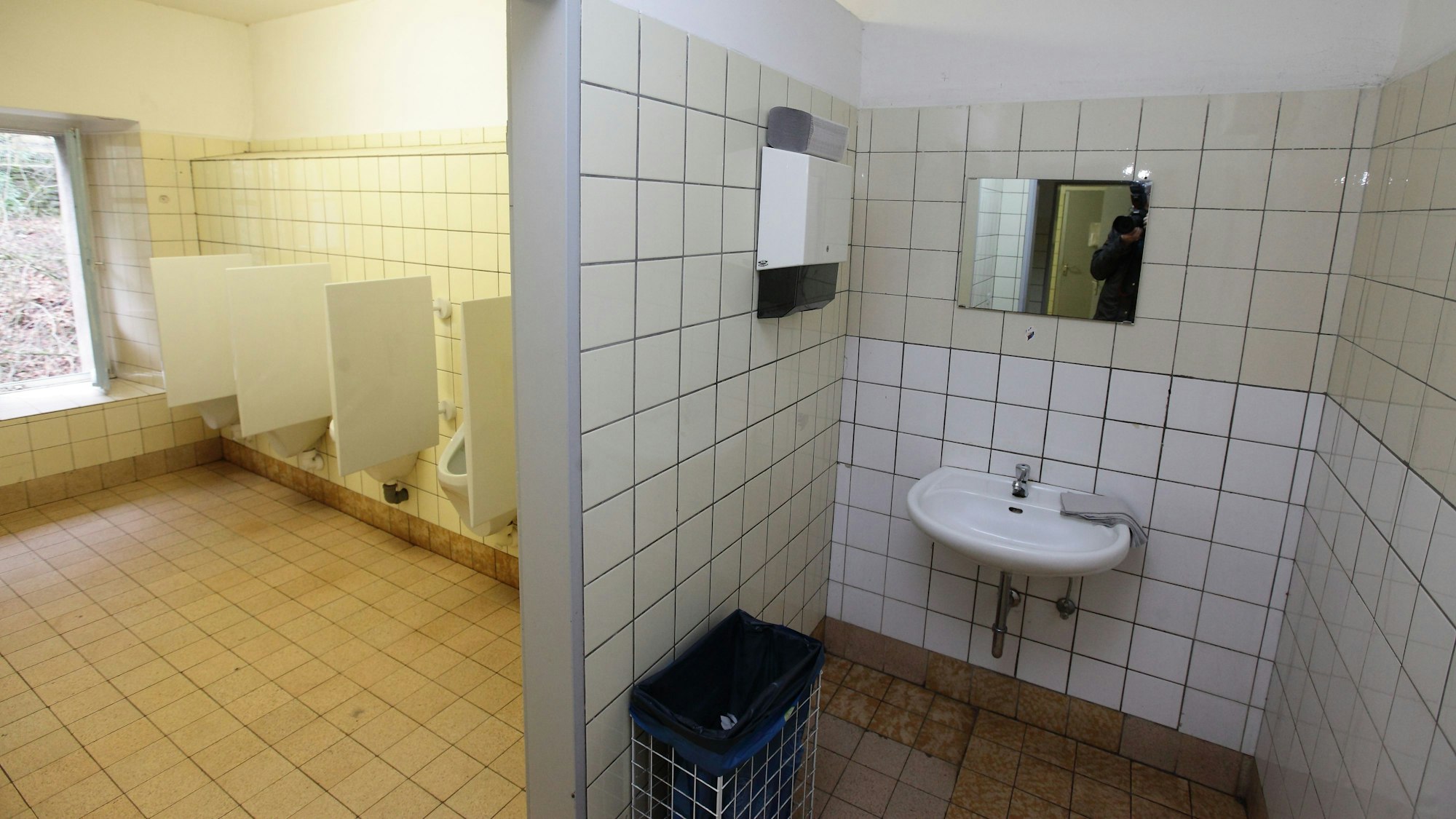 Eine alte Herrentoilette mit mehreren Urinalen und einem Waschbecken.