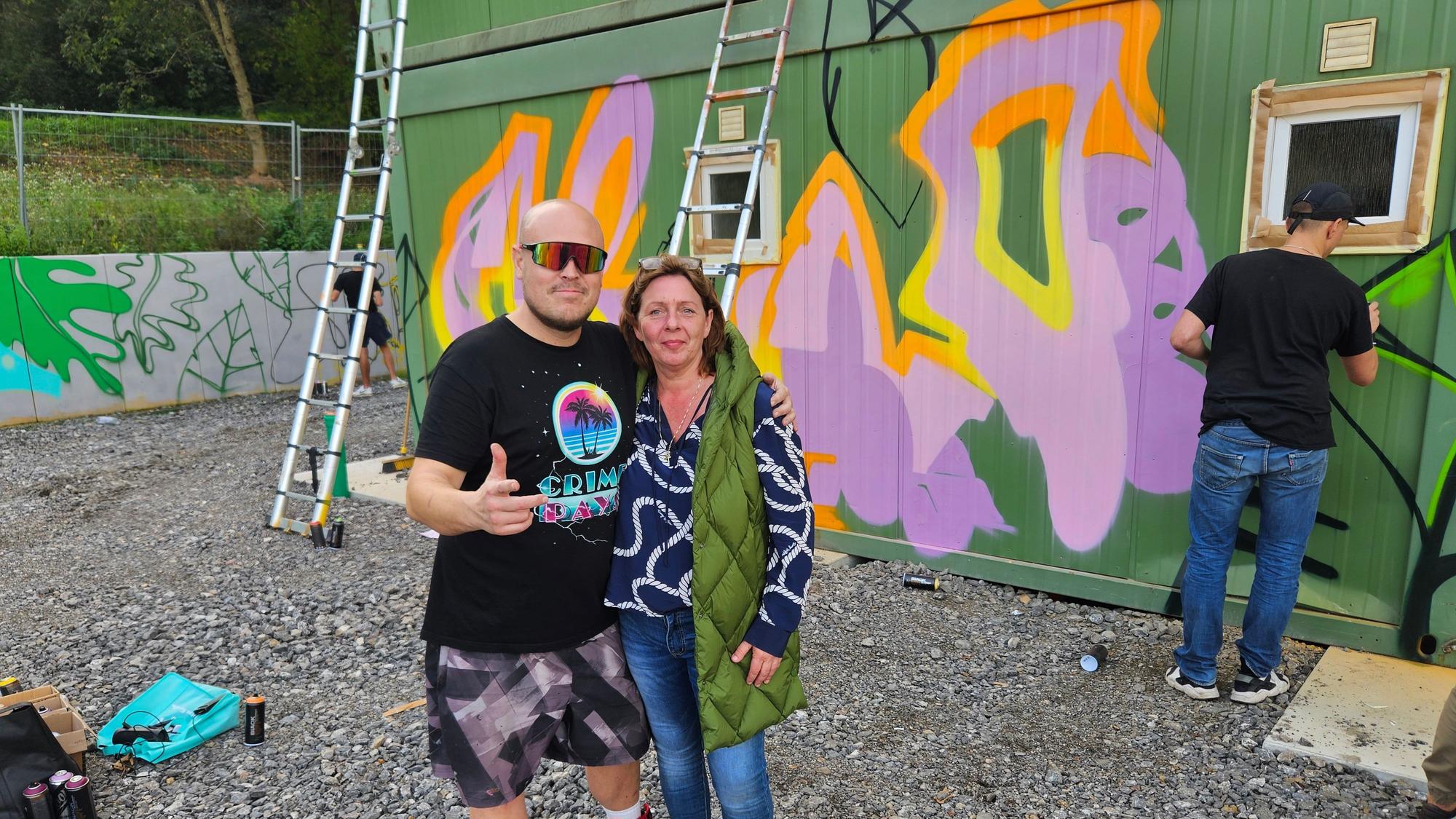 Graffiti-Künstler Henning Hüttner und Freia Johannsen von Adra soteria stehen vor den besprühten Containern.