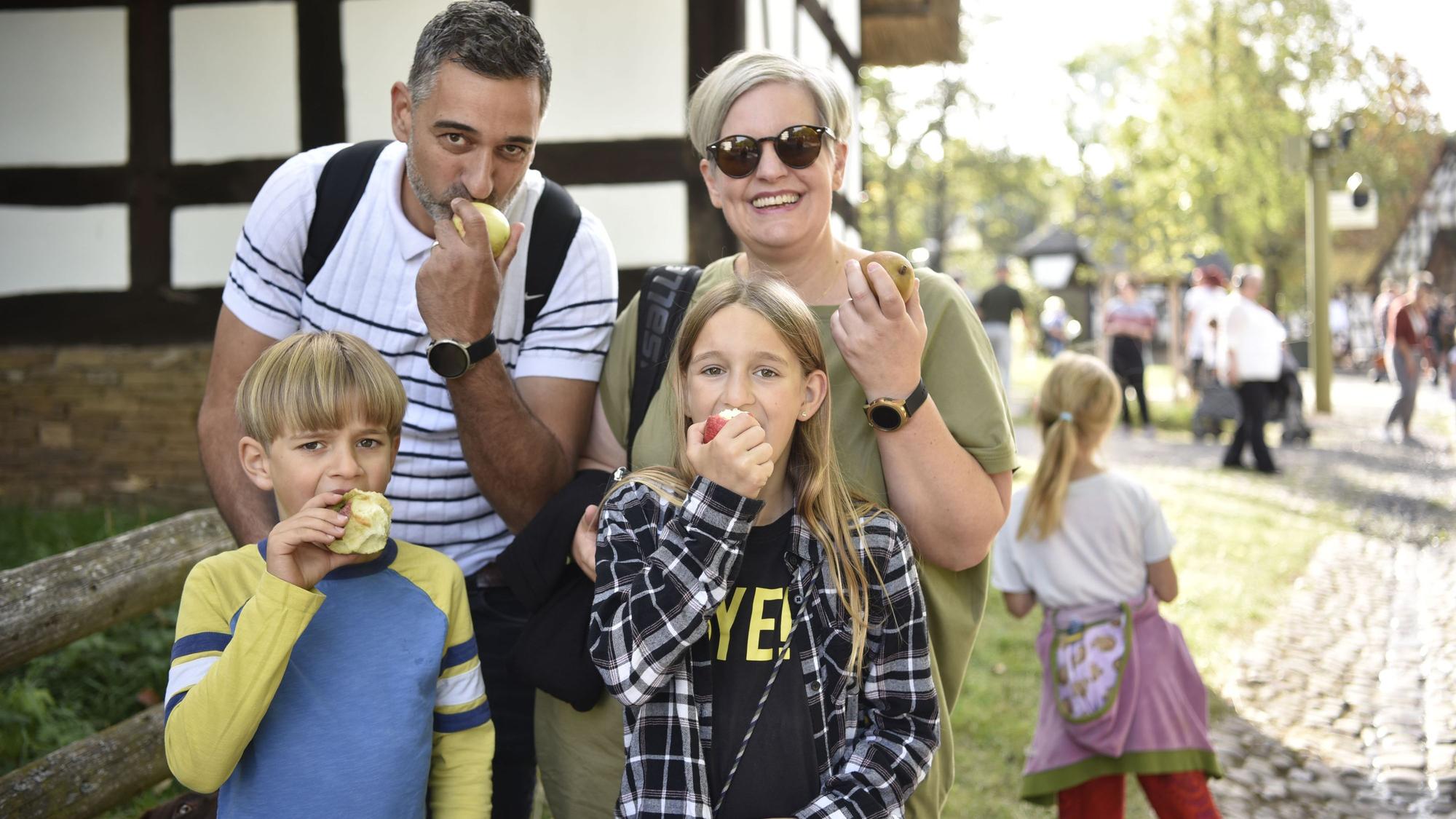 Eine Familie, Michael und Mireille Sauer sowie die Kinder Ben und Hannah, sind vor der Kulisse des Freilichtmuseums zu sehen, wie sie Äpfel probieren.