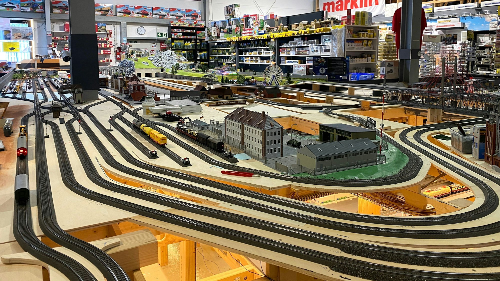 Die Modelleisenbahn-Landschaft steht in einer Halle voller Regale und Modellen.