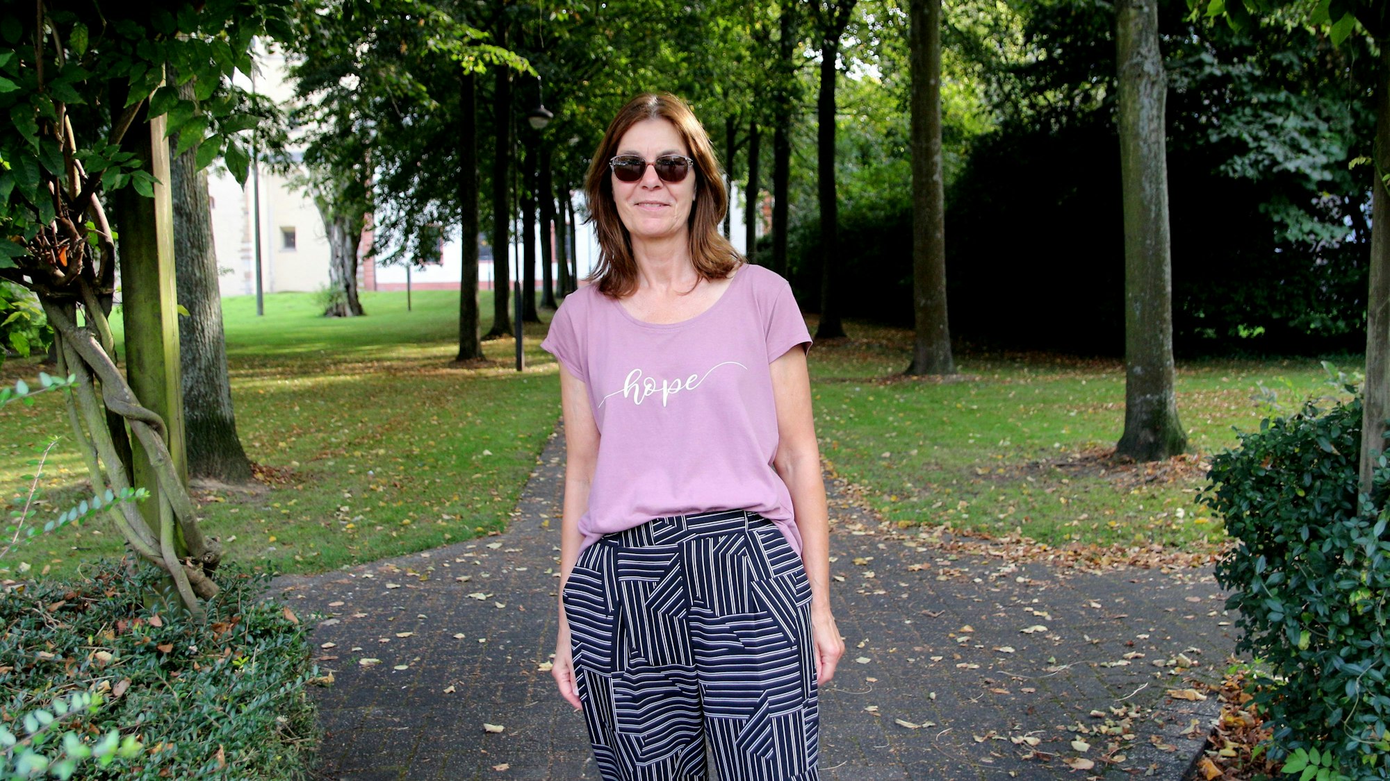 Das Foto zeigt eine Frau, sie wirkt erschöpft, verdeckt ihre Augen mit einer Sonnenbrille.