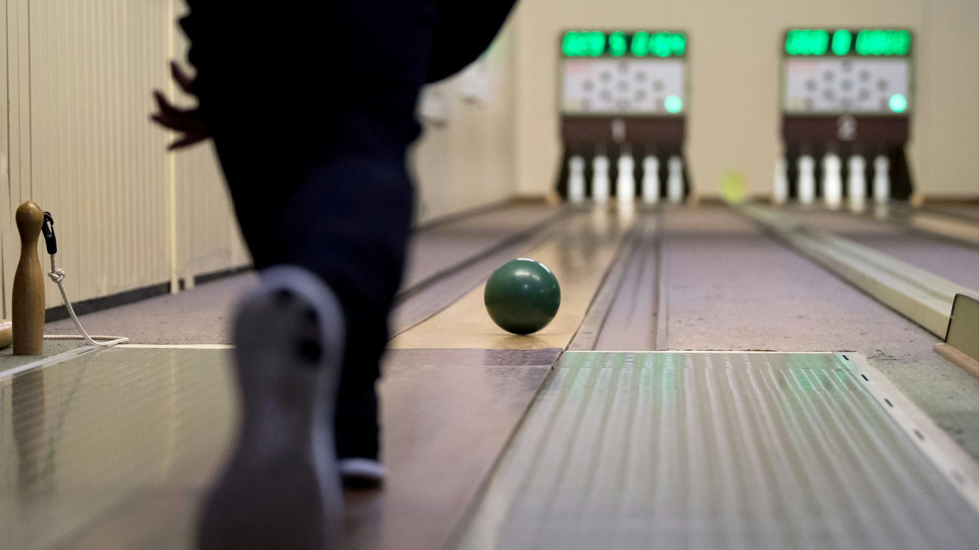 Ein Kegler rollt eine Kugel über die Lauffläche einer vollelektronischen Kegelbahn.