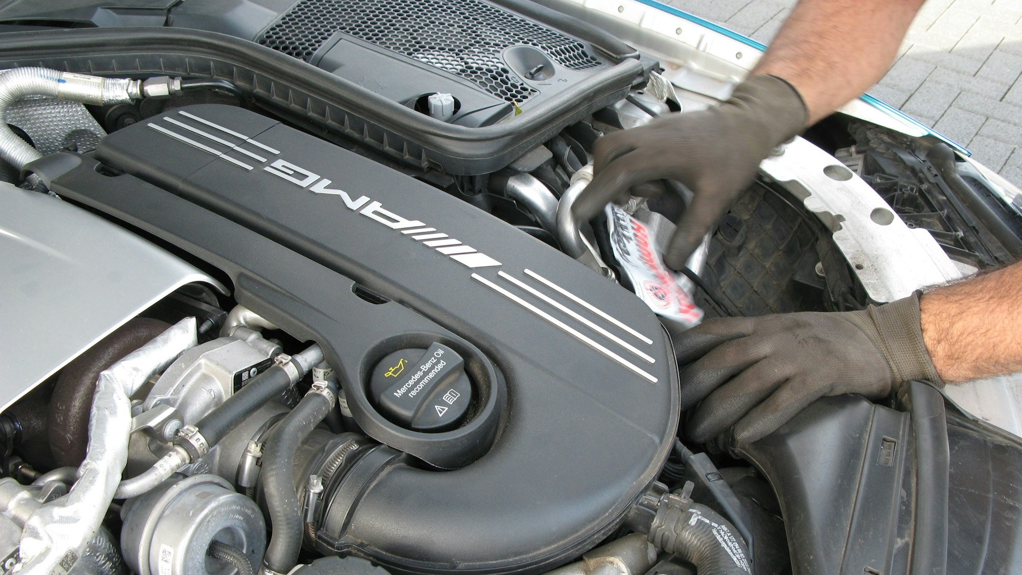 Mit Händen in dunkelgrauen Handschuhen arbeitet ein Mann an einem Automotor.