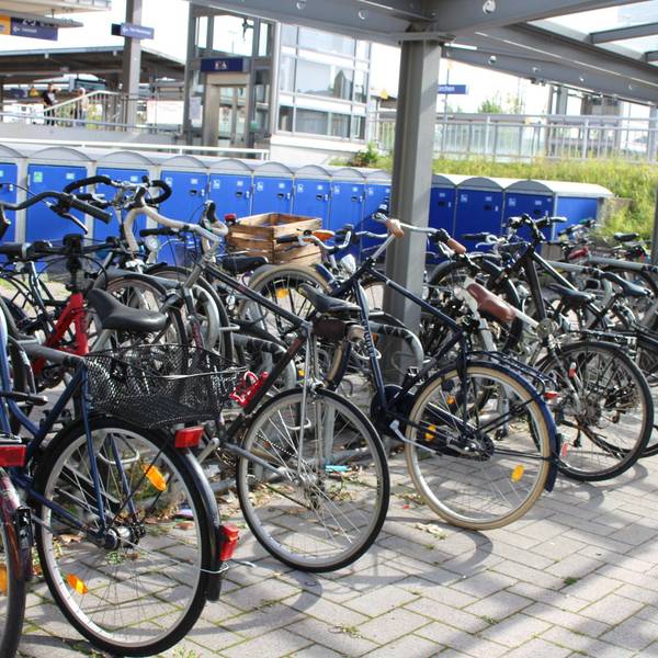 Sehr viele Fahrräder stehen in der Fahrradstation am Bahnhof, dahinter sind Boxen für Räder zu sehen.