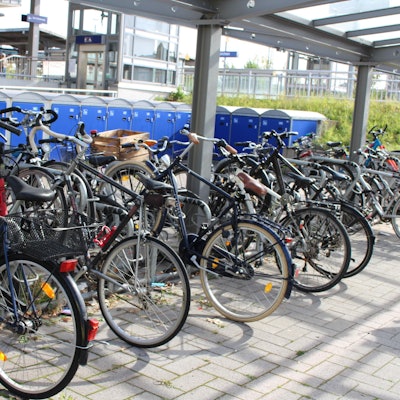Sehr viele Fahrräder stehen in der Fahrradstation am Bahnhof, dahinter sind Boxen für Räder zu sehen.