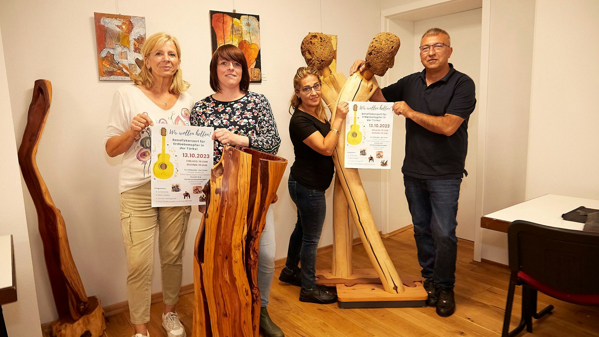 In einem Raum mit Holzskulpturen stehen die Veranstalter des Benefizkonzerts. Gaby Hess (v.l.), Lotte Ackermann-Vandeweyer, Serpil Yildiz und Yasin Yildiz halten die Plakate in den Händen.