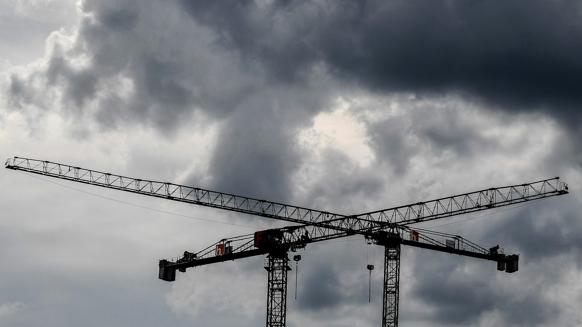 Baukräne sind vor dunklen Wolken zu sehen. (Symbolbild)