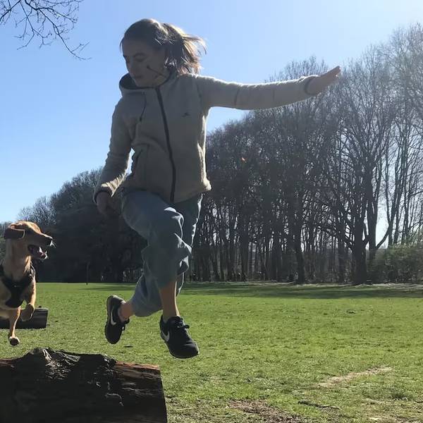Ein Hund springt mit seiner Trainerin über einen Baumstamm