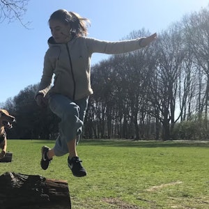 Ein Hund springt mit seiner Trainerin über einen Baumstamm