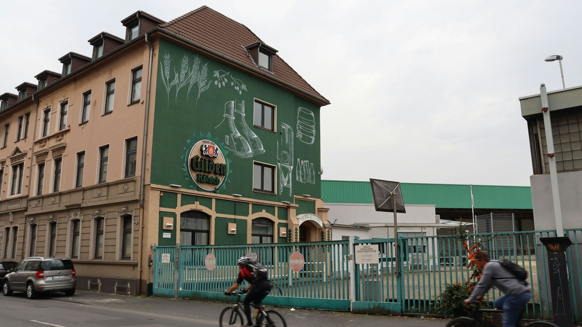 Die Gilden-Brauerei mit einer Straße und zwei Fahrradfahrer im Vordergrund.