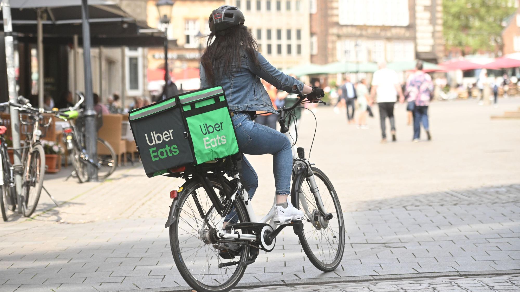 Eine Lieferantin fährt auf einem Fahrrad mit Uber Eats Gepäcktasche.