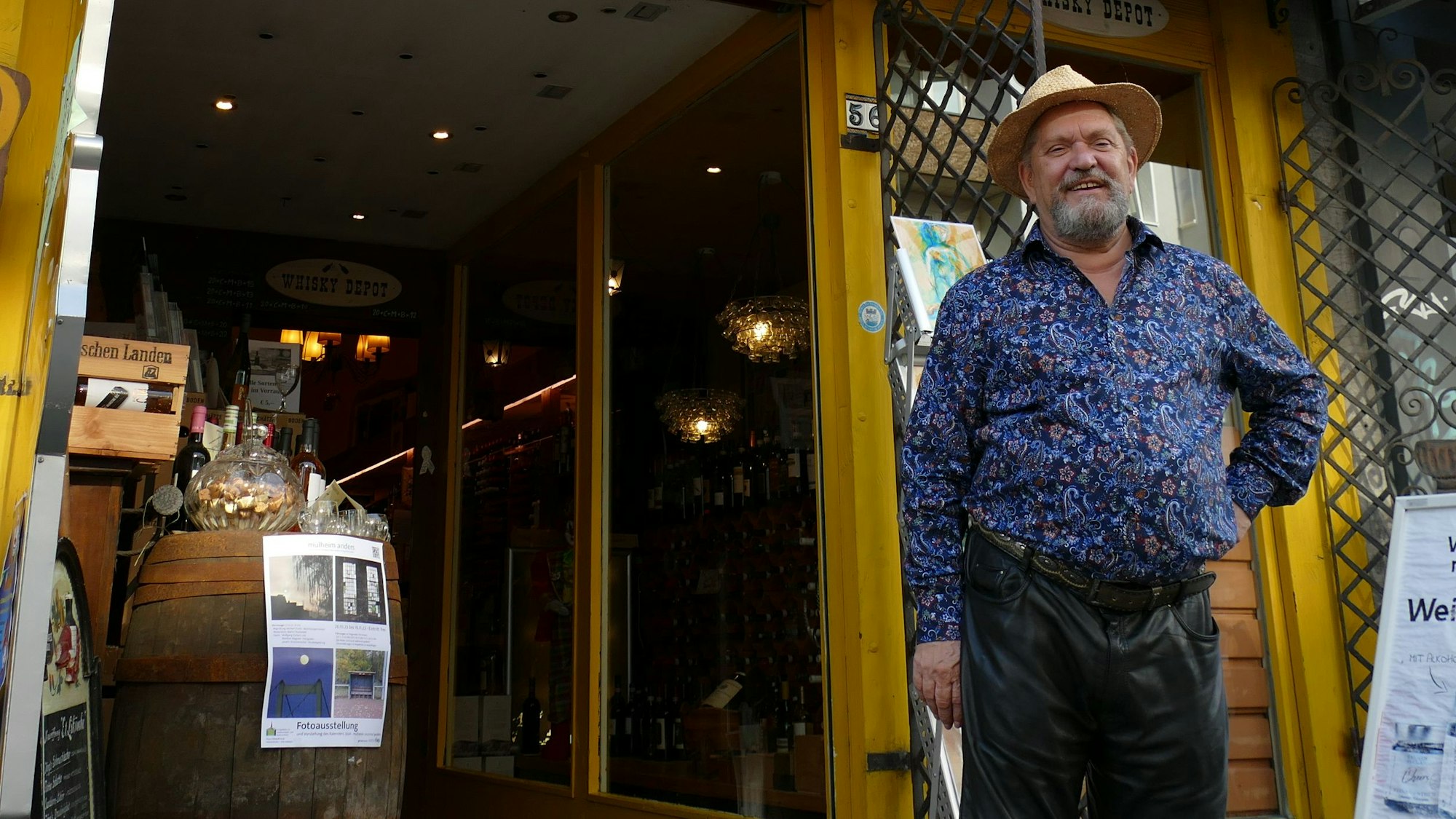 Ein Mann mit Hut und buntem Hemd steht vor einem Geschäft mit gelbem Eingang.