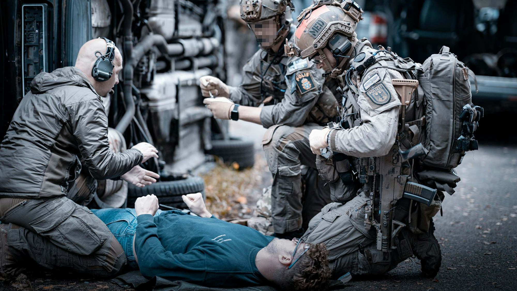 Spezialkräfte in voller Kampfmontur versorgen einen auf dem Boden liegenden Zivilisten, der einen Verletzten darstellt.