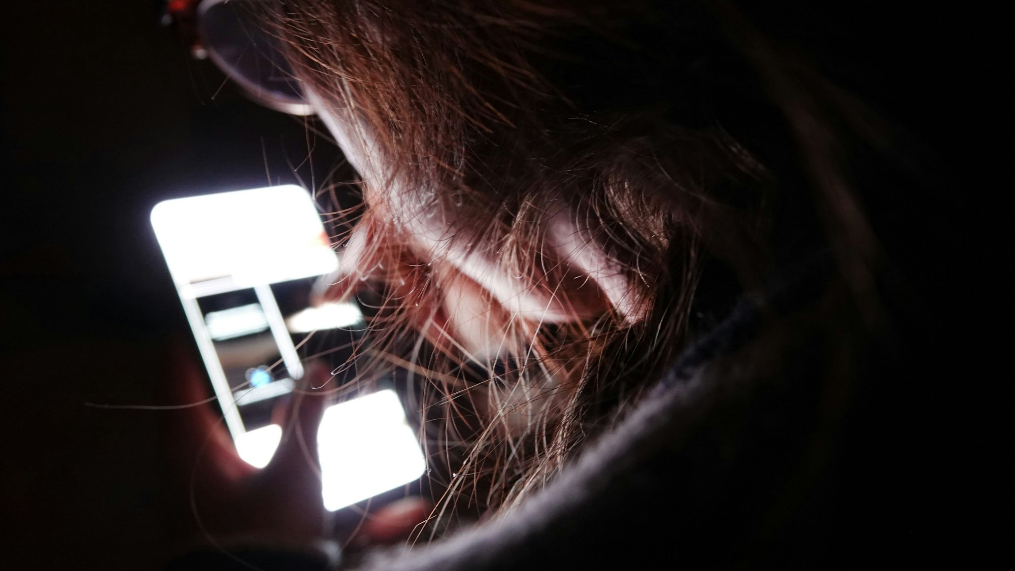 Ein Kind schaut im Dunkeln auf ein Handybildschirm.