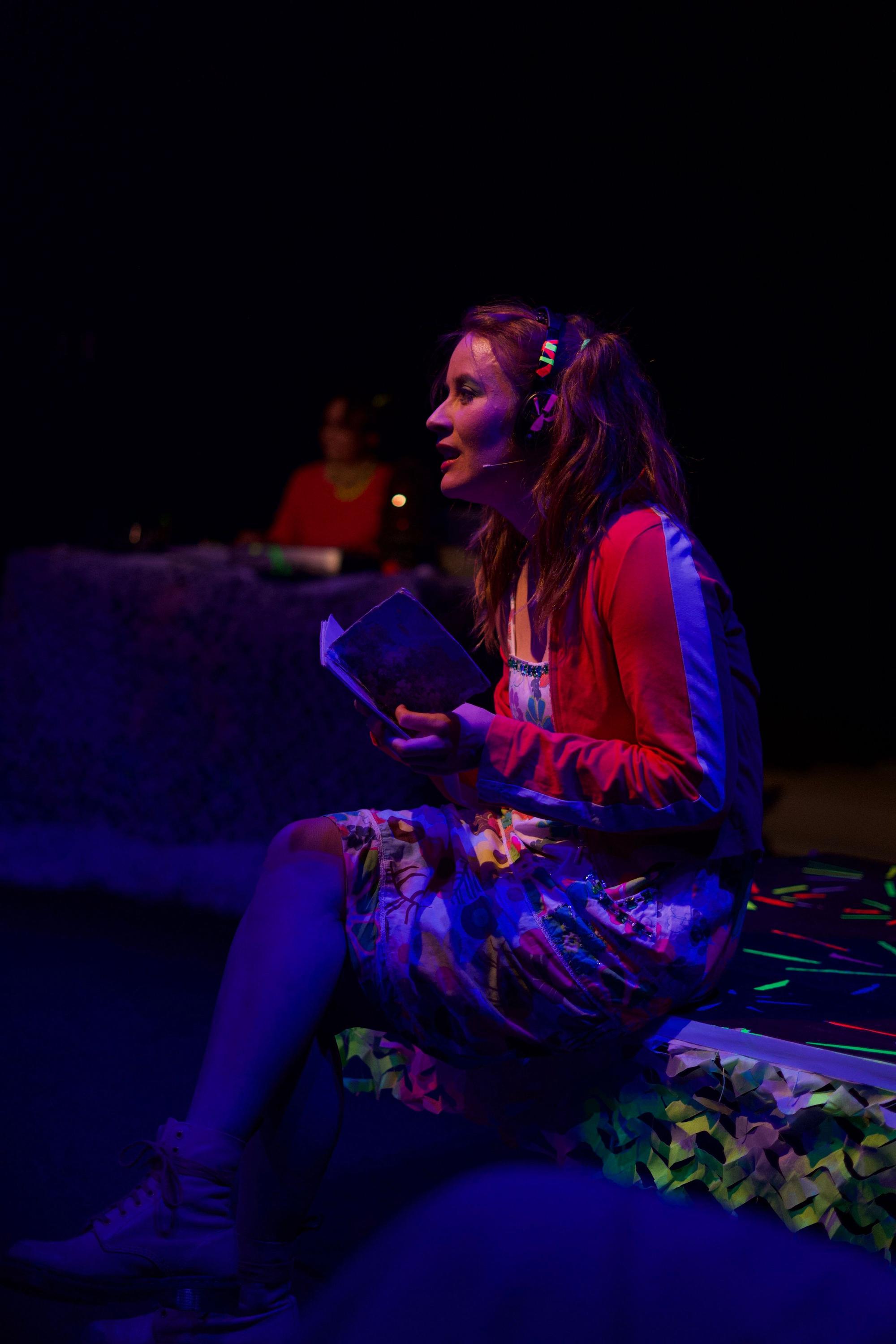 In der Dunkelheit sorgt ein blaues Neonlicht für ein paar Konturen. Die Schauspielerin Lucia Schulz sitzt auf der Bühne, sie hat ein Buch in der Hand.