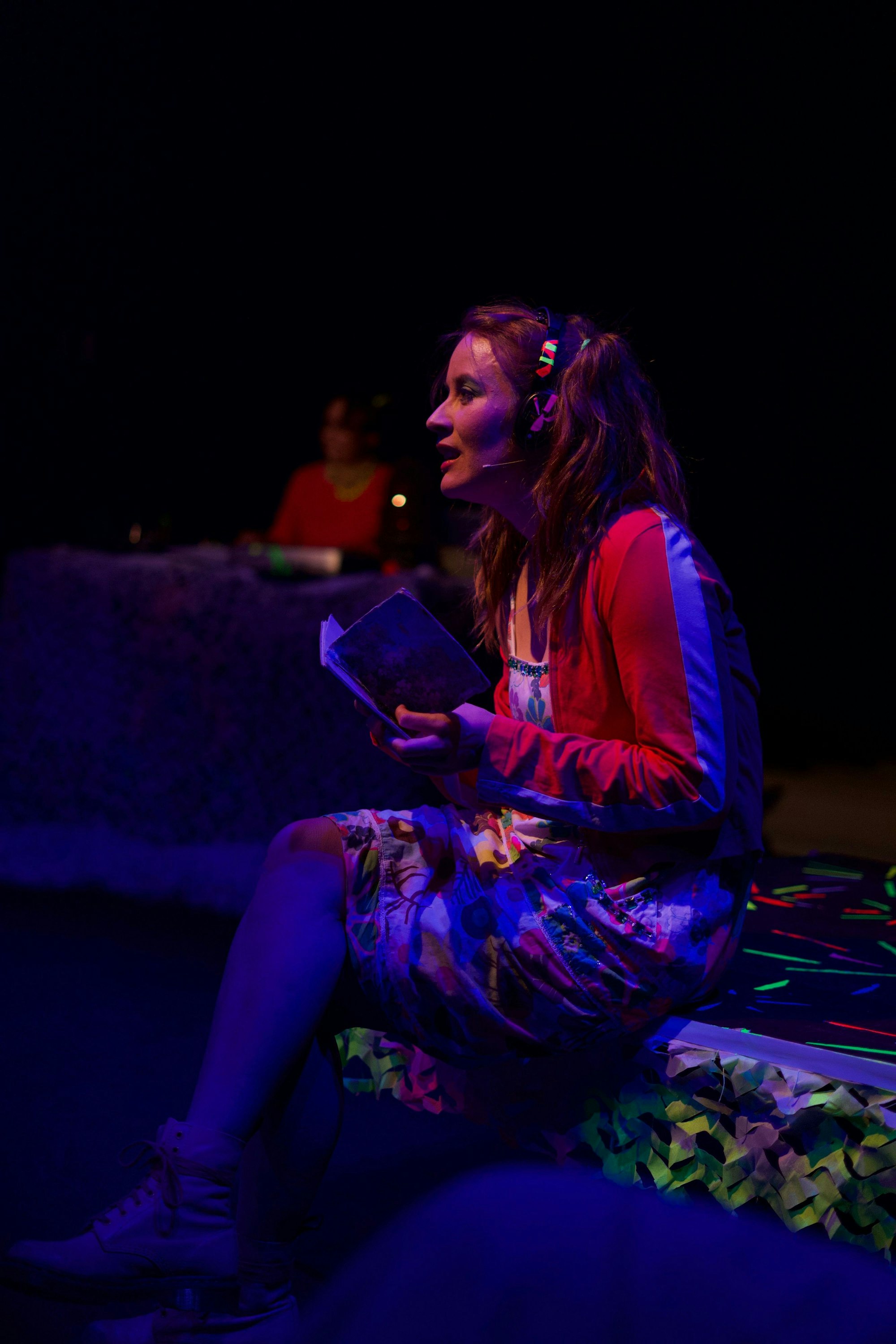 In der Dunkelheit sorgt ein blaues Neonlicht für ein paar Konturen. Die Schauspielerin Lucia Schulz sitzt auf der Bühne, sie hat ein Buch in der Hand.