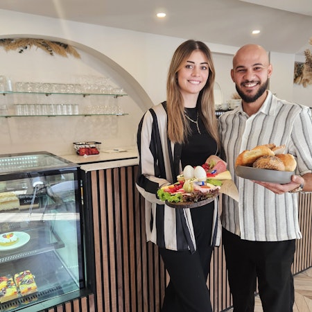 Linda und Ramadan Ajdini präsentieren vor der Theke ein Frühstück für zwei Personen.
