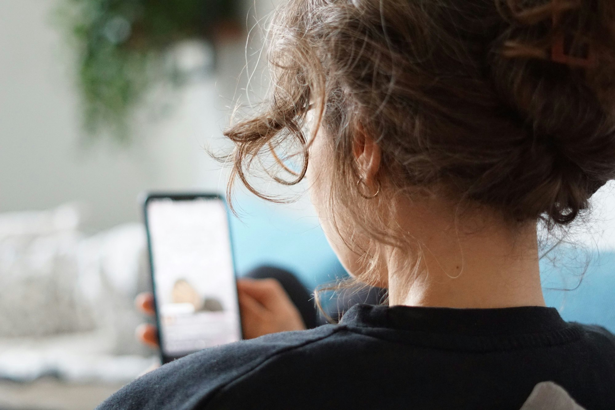 Eine Frau sitzt auf einem Sofa und schaut sich ein Video auf der Social-Media-Plattform Instagram auf ihrem Handy an.
