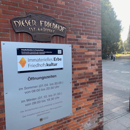 Das Foto zeigt den Eingang zum Friedhof mit der Tafel, die auf die Mitgliedschaft in der Charta hinweist.