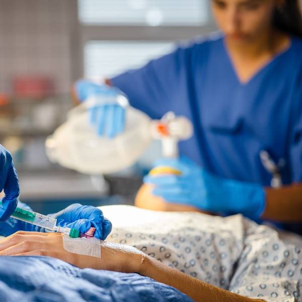 Jemand spitzt einem Patienten etwas in eine Kanüle.