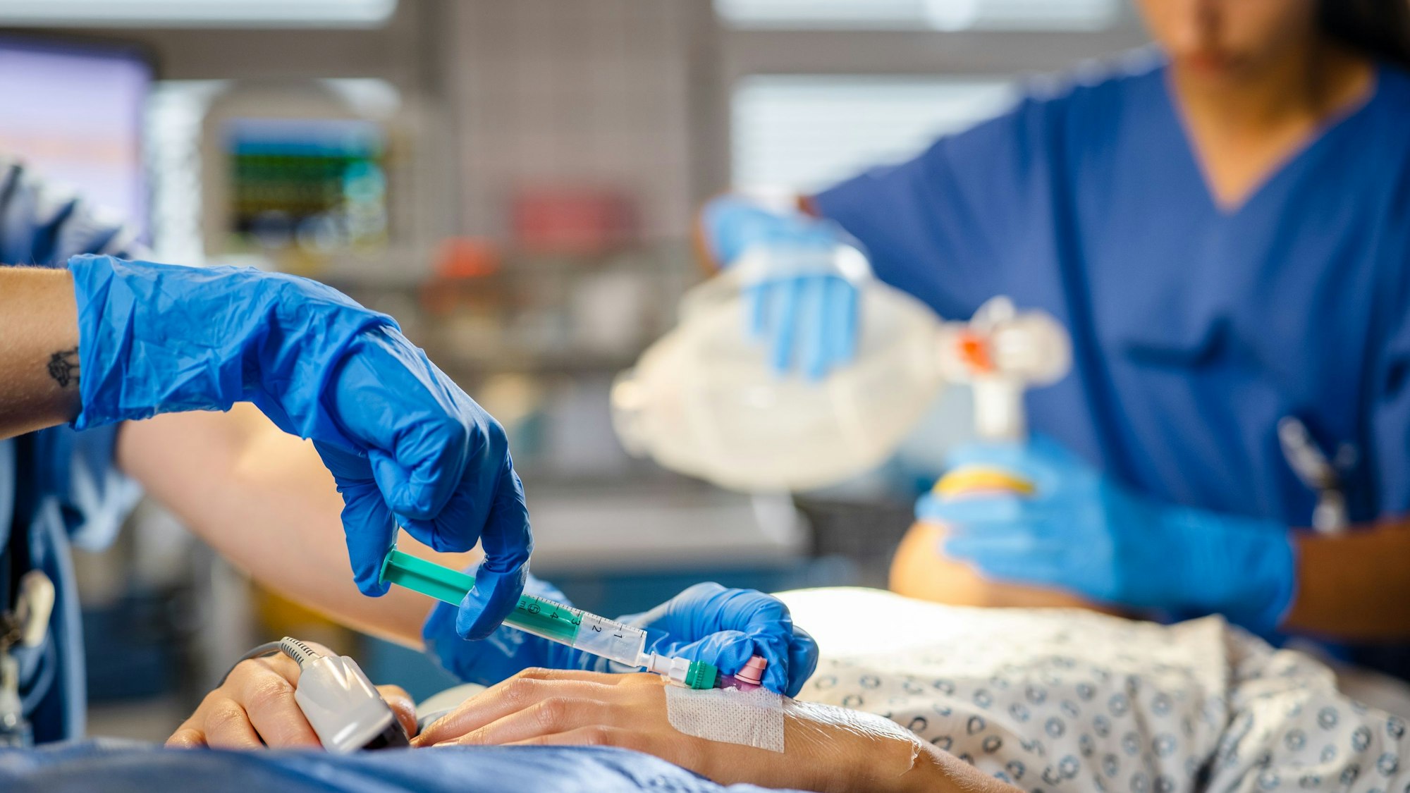 Jemand spitzt einem Patienten etwas in eine Kanüle.