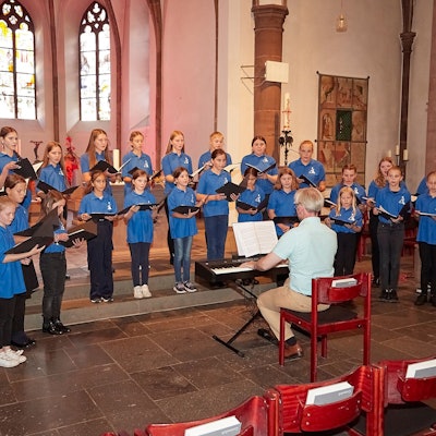 Der Mädchenchor aus Kevelaer steht im Altarraum der Marmagener Kirche und singt. Der Leiter Romano Giefer sitzt davor an einem Keyboard.