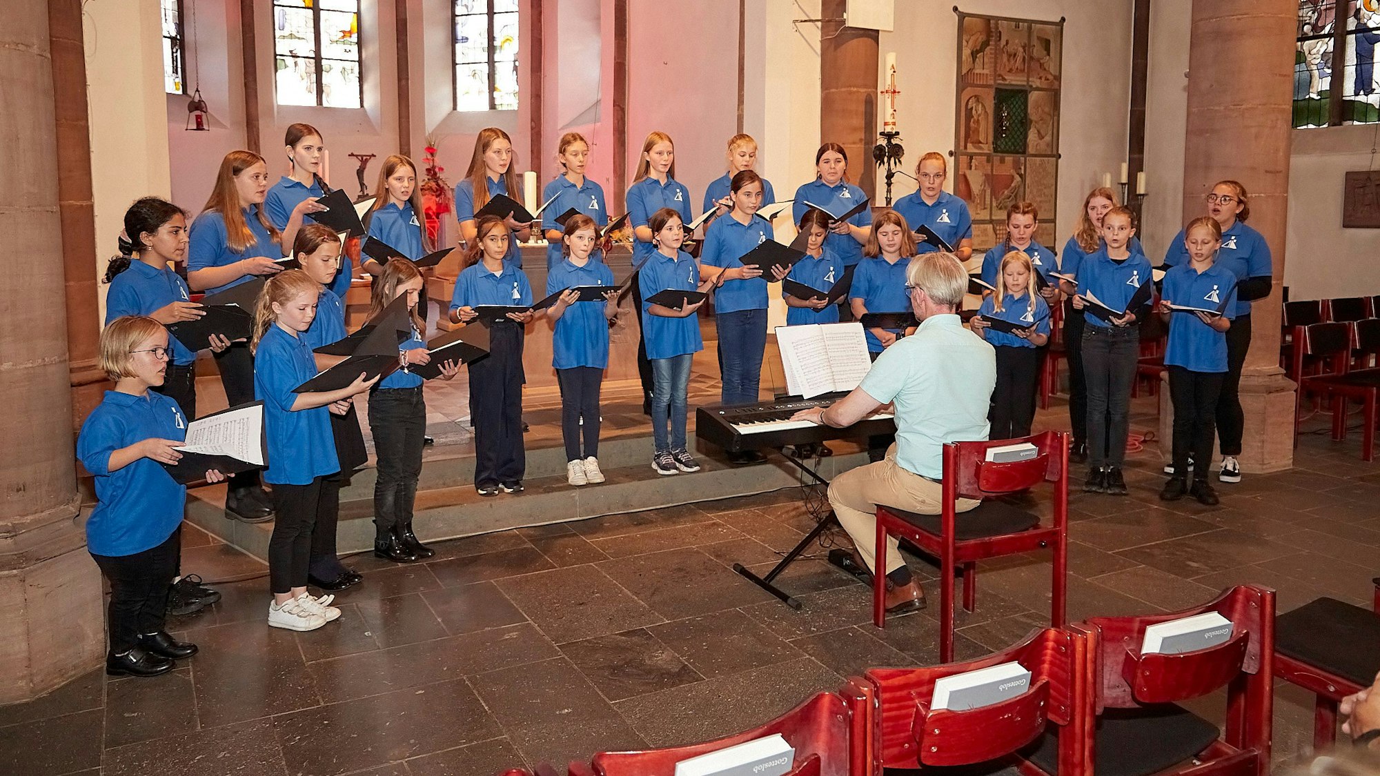 Der Mädchenchor aus Kevelaer steht im Altarraum der Marmagener Kirche und singt. Der Leiter Romano Giefer sitzt davor an einem Keyboard.