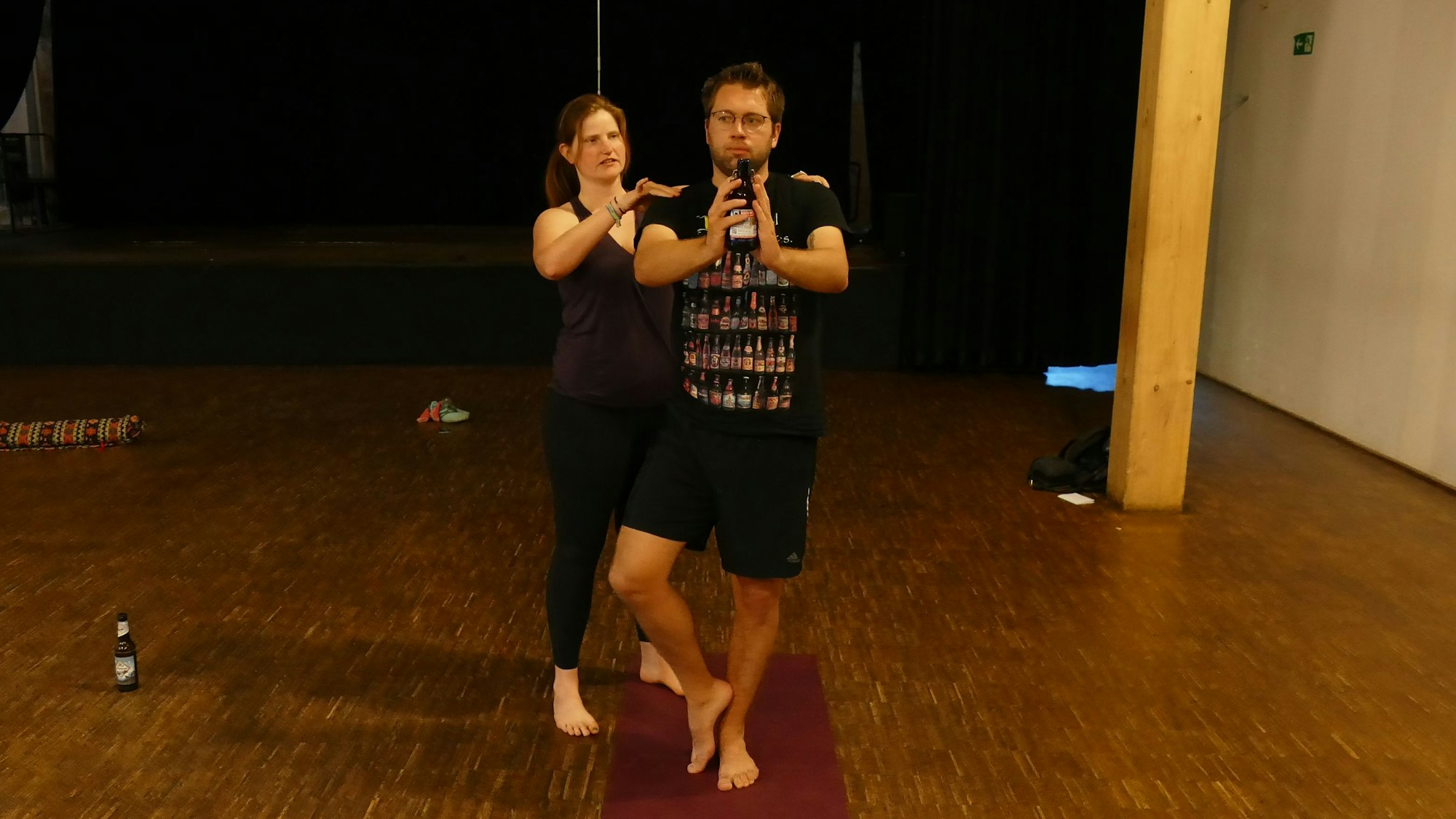 Alina Berg hält ihre Hände auf Marius Fuhrmanns Schultern, während er eine Flasche Bier mit seinen Handinnenflächen hält.