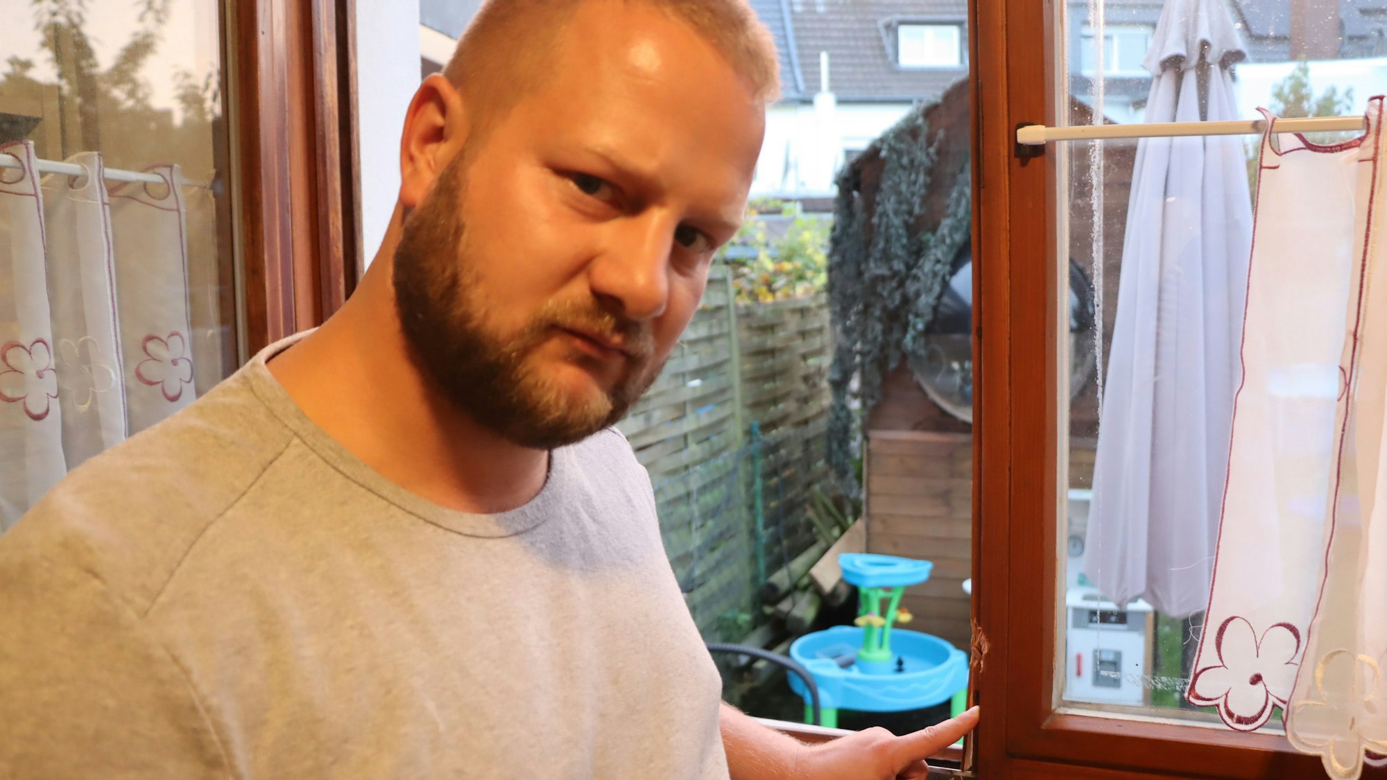 Auf dem Foto ist Tobias Pohl zu sehen. Das Einbruchsopfer zeigt auf einen beschädigten Fensterrahmen.