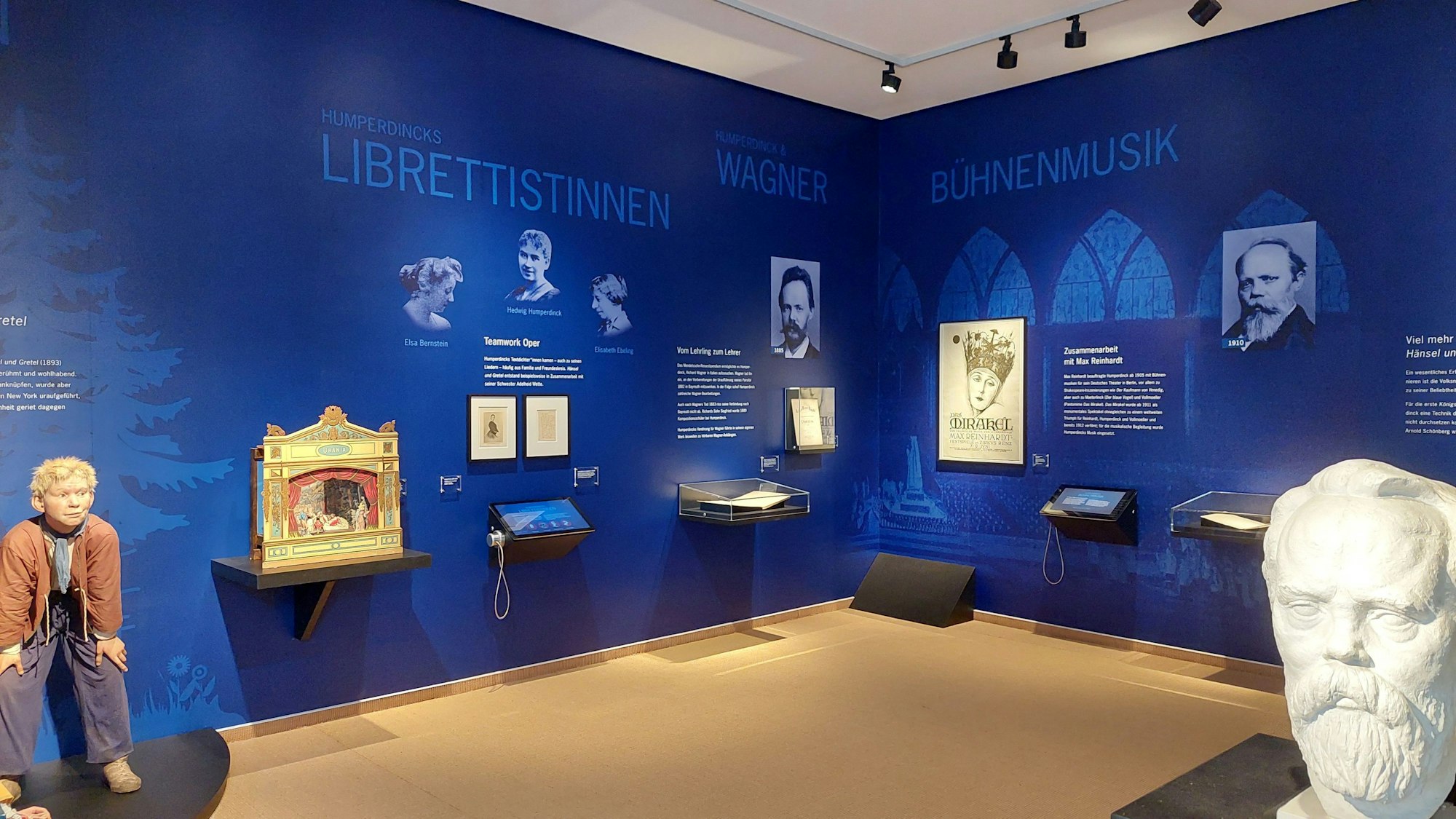 Neue Humperdinck-Abteilung im Stadtmuseum Siegburg. Zu sehen ist die Ausstellung. An großen blauen Wänden stehen Texte und Bilder, etwa der Librettistinnen seiner Stücke. An den Wänden hängen auch einige Bildschirme mit Kopfhörern.