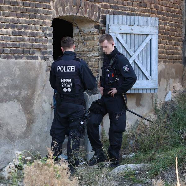 Zwei Polizisten stehen am Eingang einer Halle. Dort wurde eine Cannabisplantage gefunden.