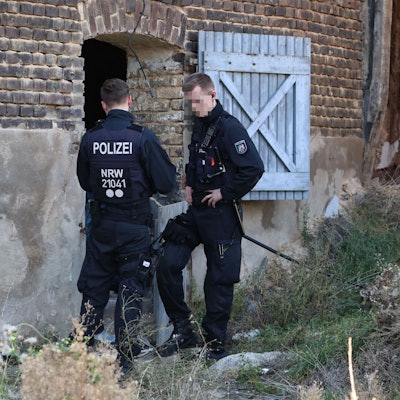 Zwei Polizisten stehen am Eingang einer Halle. Dort wurde eine Cannabisplantage gefunden.