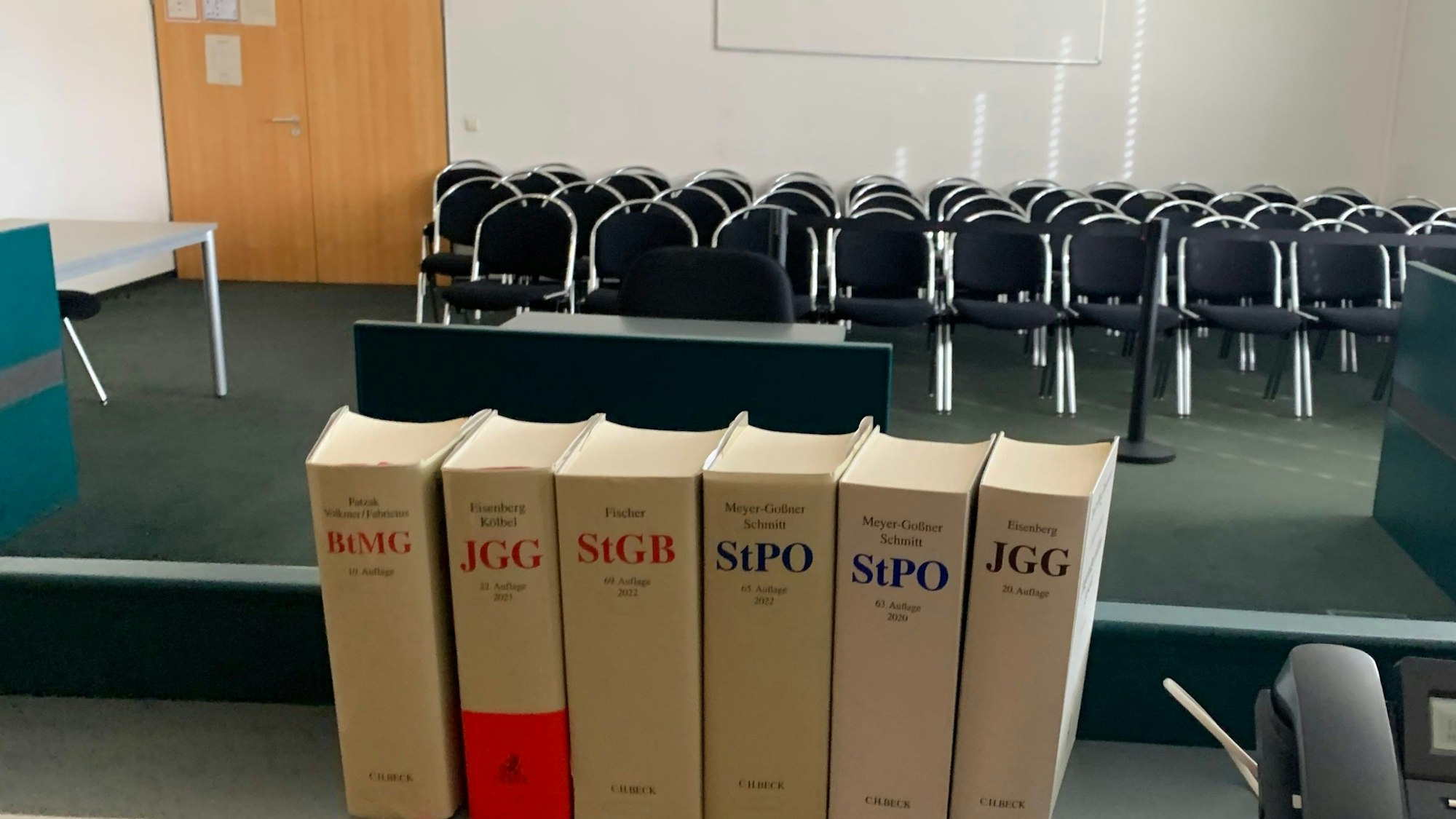 Das Symbolbild zeigt einen Gerichtssaal und im Vordergrund Bücher mit Gesetzestexten.