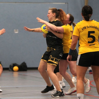 Eine Handballspielerin hat den Ball, eine Gegnerin umklammert sie von hinten.