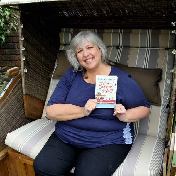 Eine Frau sitzt in einem Strandkorb und hält ein Buch in der Hand.
