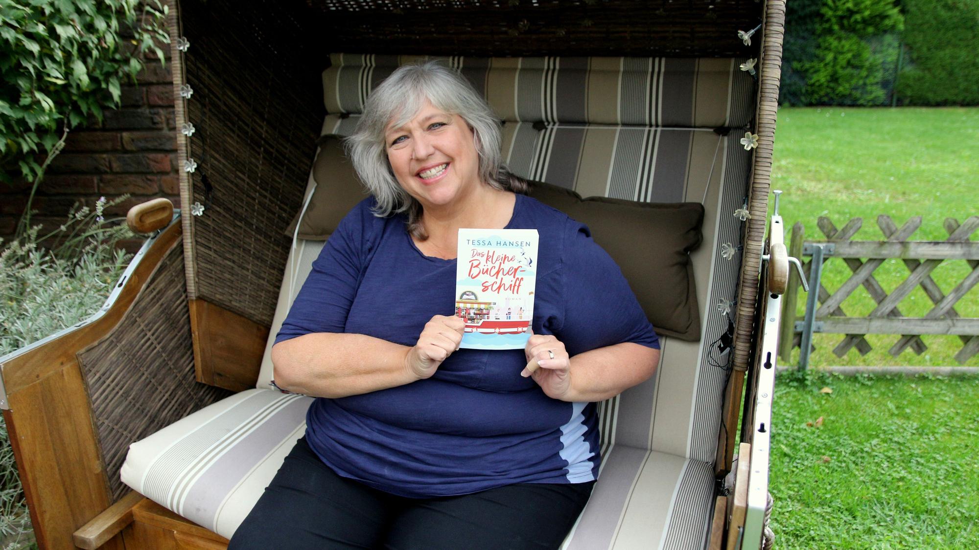 Eine Frau sitzt in einem Strandkorb und hält ein Buch in der Hand.