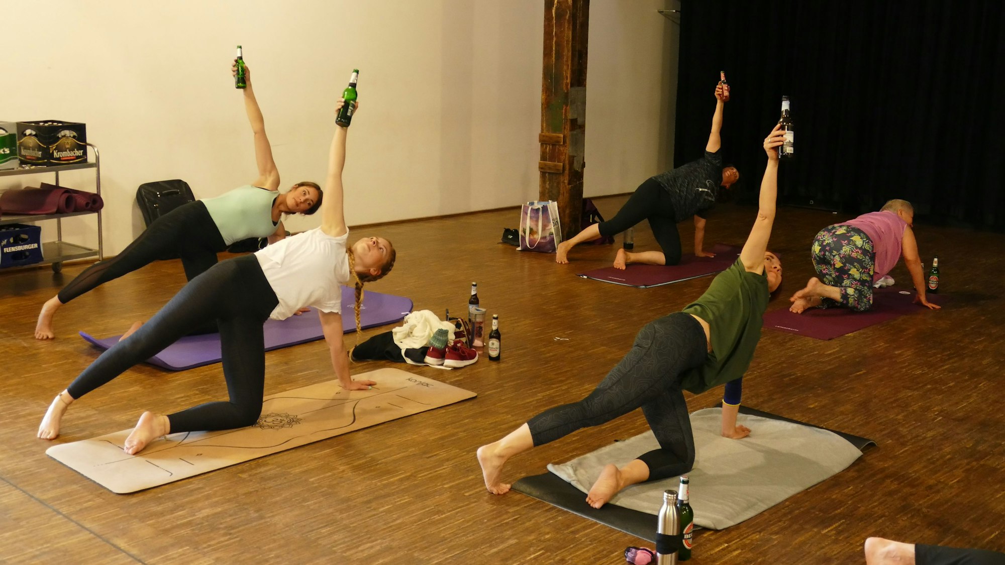 Teilnehmer stützen sich auf der Yogamatte ab und recken mit der anderen Hand eine Bierflasche in die Höhe.