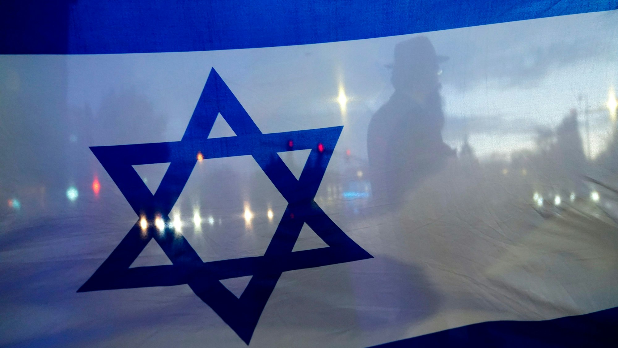 In einer Israel-Flagge spiegeln sich Lichter und Menschen.