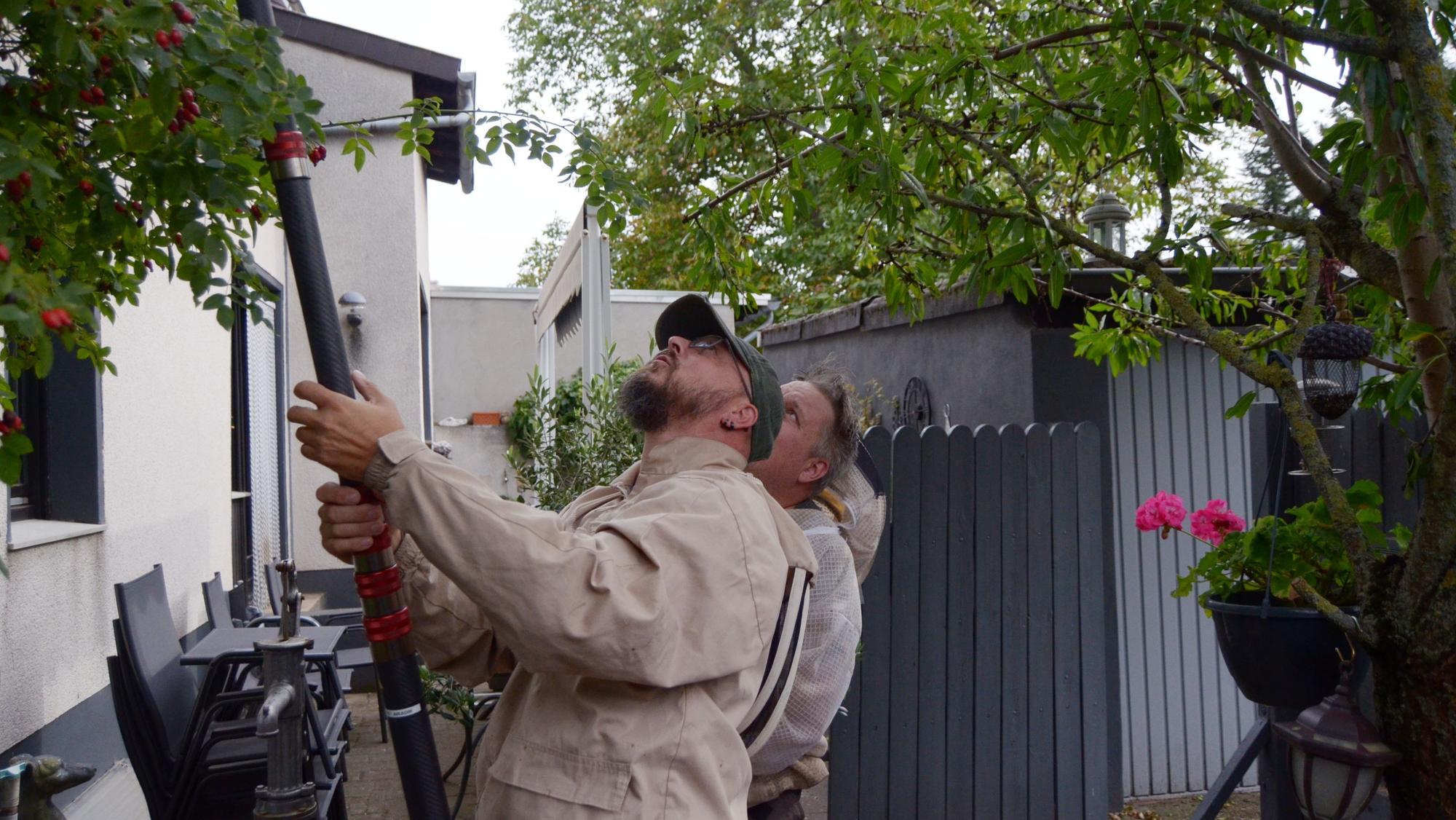 Zwei Männer stehen vor einem Haus und schauen nach oben. Einer hält ein Rohr in den Händen.